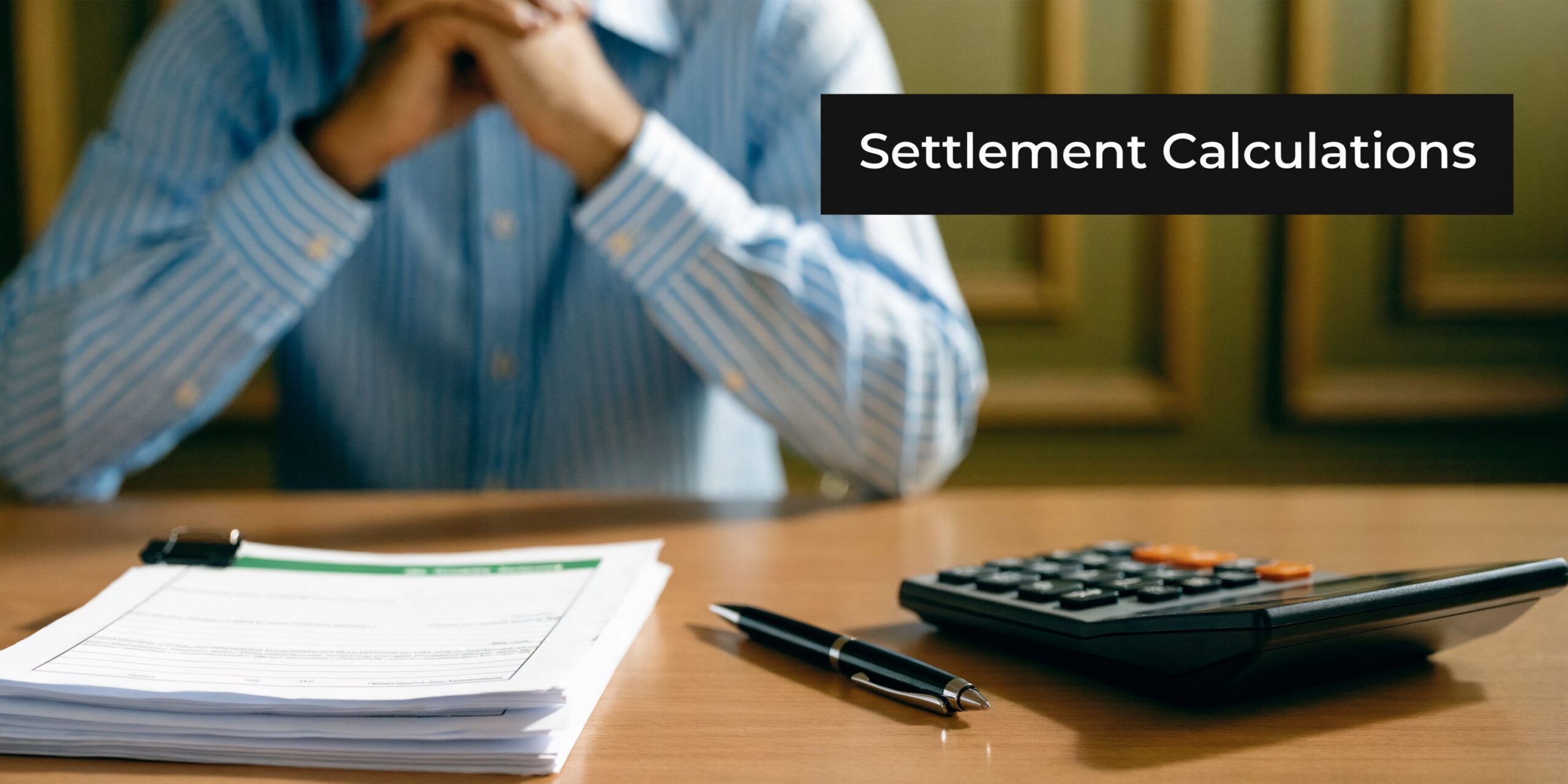 A professional sitting at a desk with paperwork, a calculator, and a pen for settlement calculations.