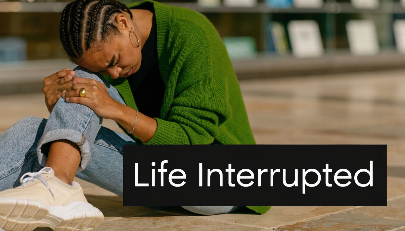 A young woman in a green cardigan sits on the ground in distress, clutching her injured knee.