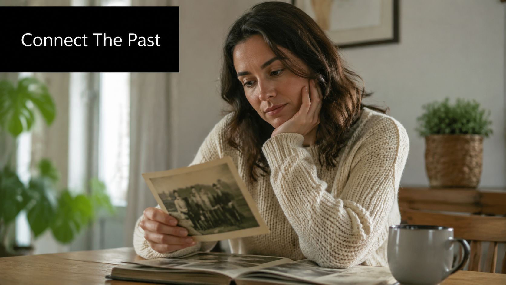 A woman looks at an old black and white photograph while sitting at a table with memories.